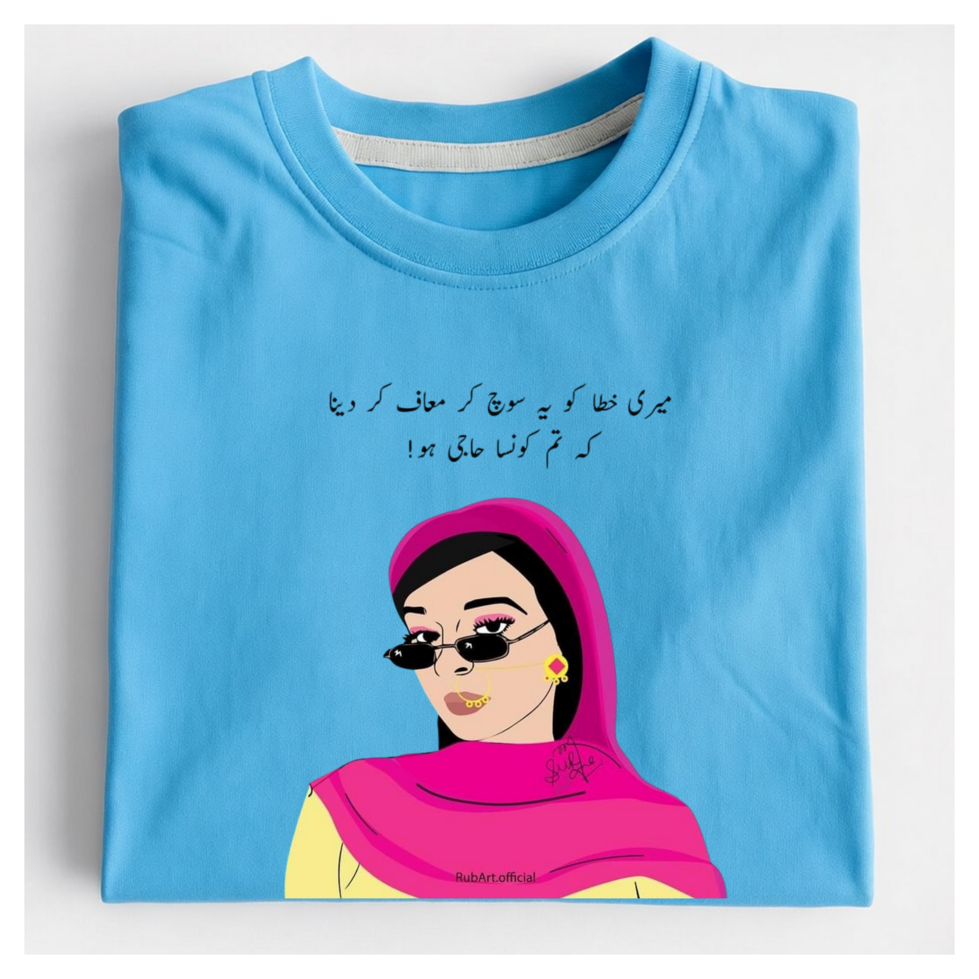 A folded light blue t-shirt with a graphic print of a woman in a pink headscarf and sunglasses, accompanied by black Urdu script, displayed on a clean white background.