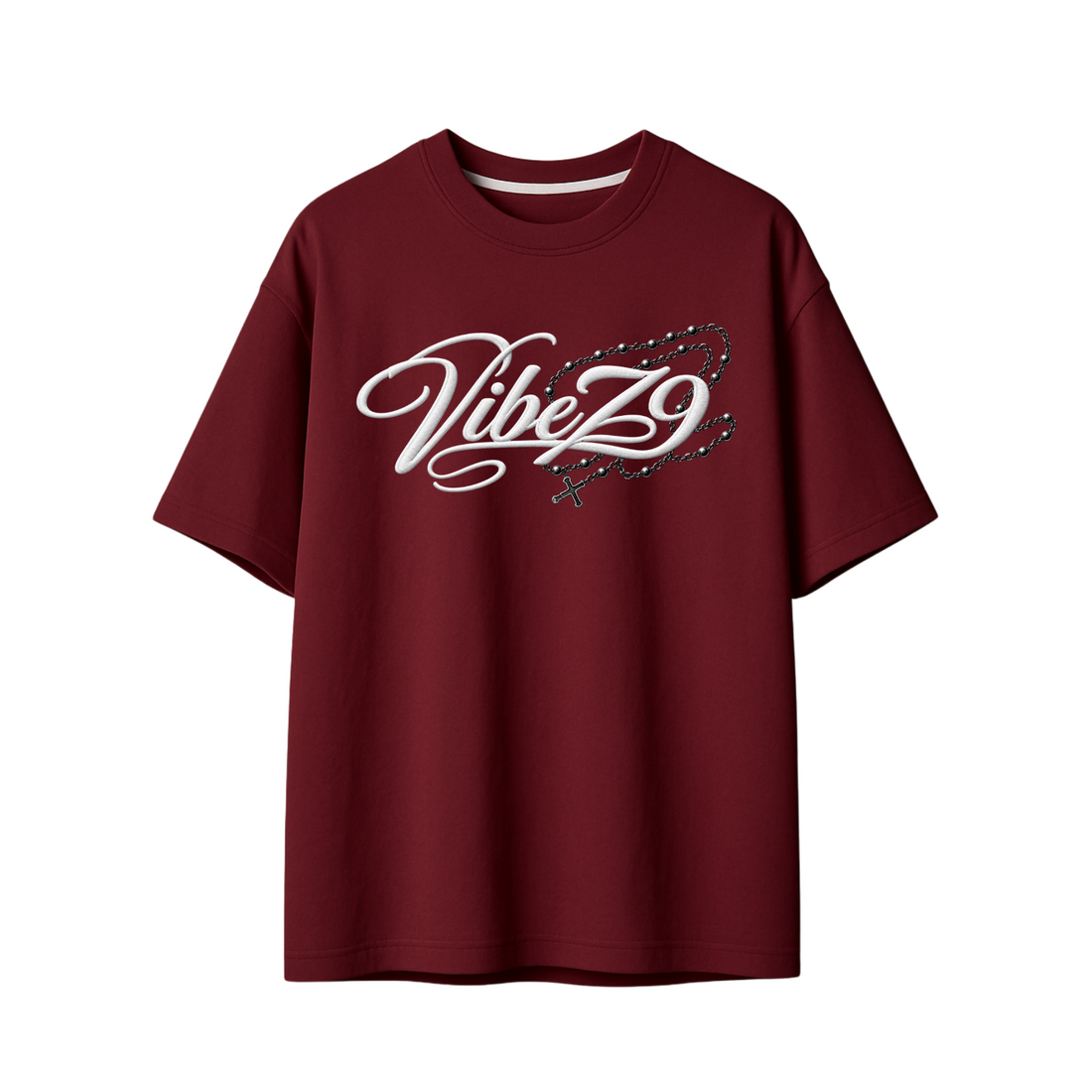 A maroon short-sleeve t-shirt featuring a large, detailed graphic of a silver gothic-style rosary with skull and cross details printed on the front, set against a plain white background.