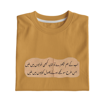 A folded mustard yellow t-shirt with a printed beige graphic containing black Urdu calligraphy, displayed on a solid white background.