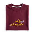 A folded maroon crewneck t-shirt with yellow and white Urdu script printed on the front, displayed against a plain white background.