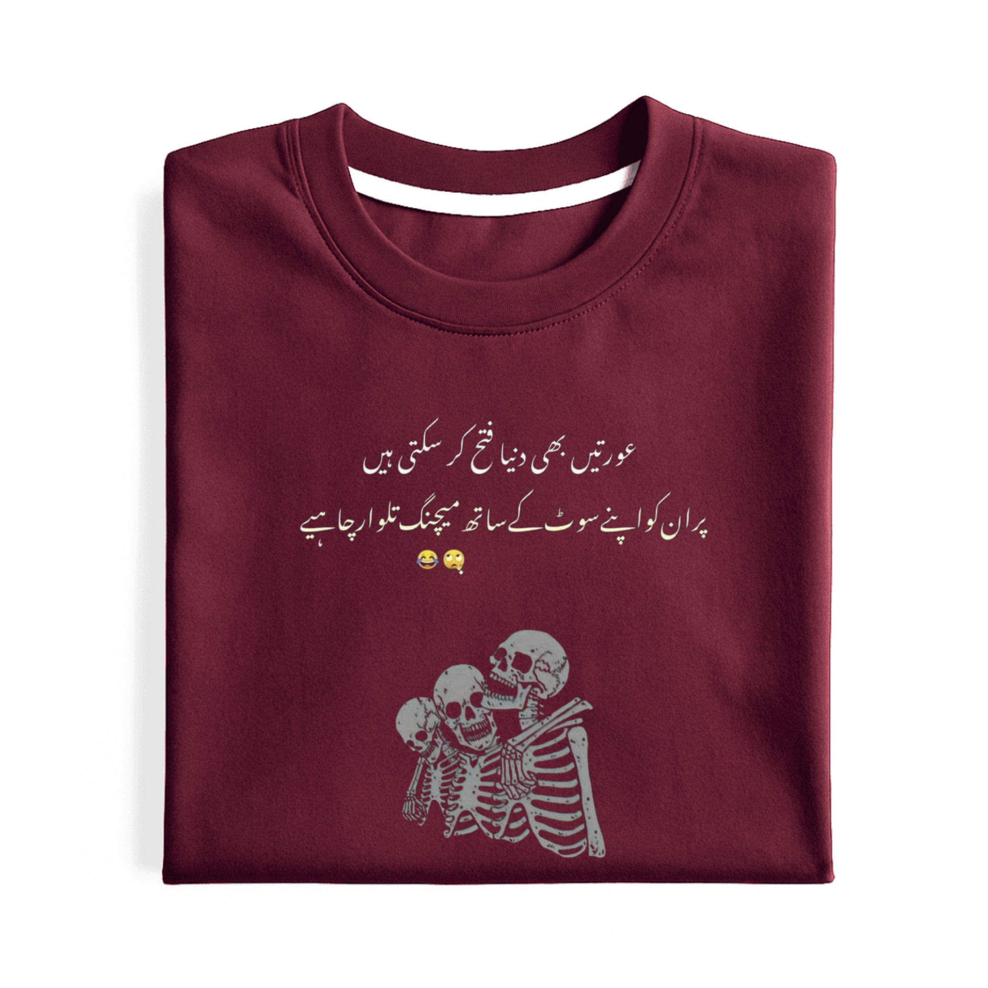 A folded maroon crewneck t-shirt with white Urdu text and a white skeleton graphic on the front, displayed on a clean white background.