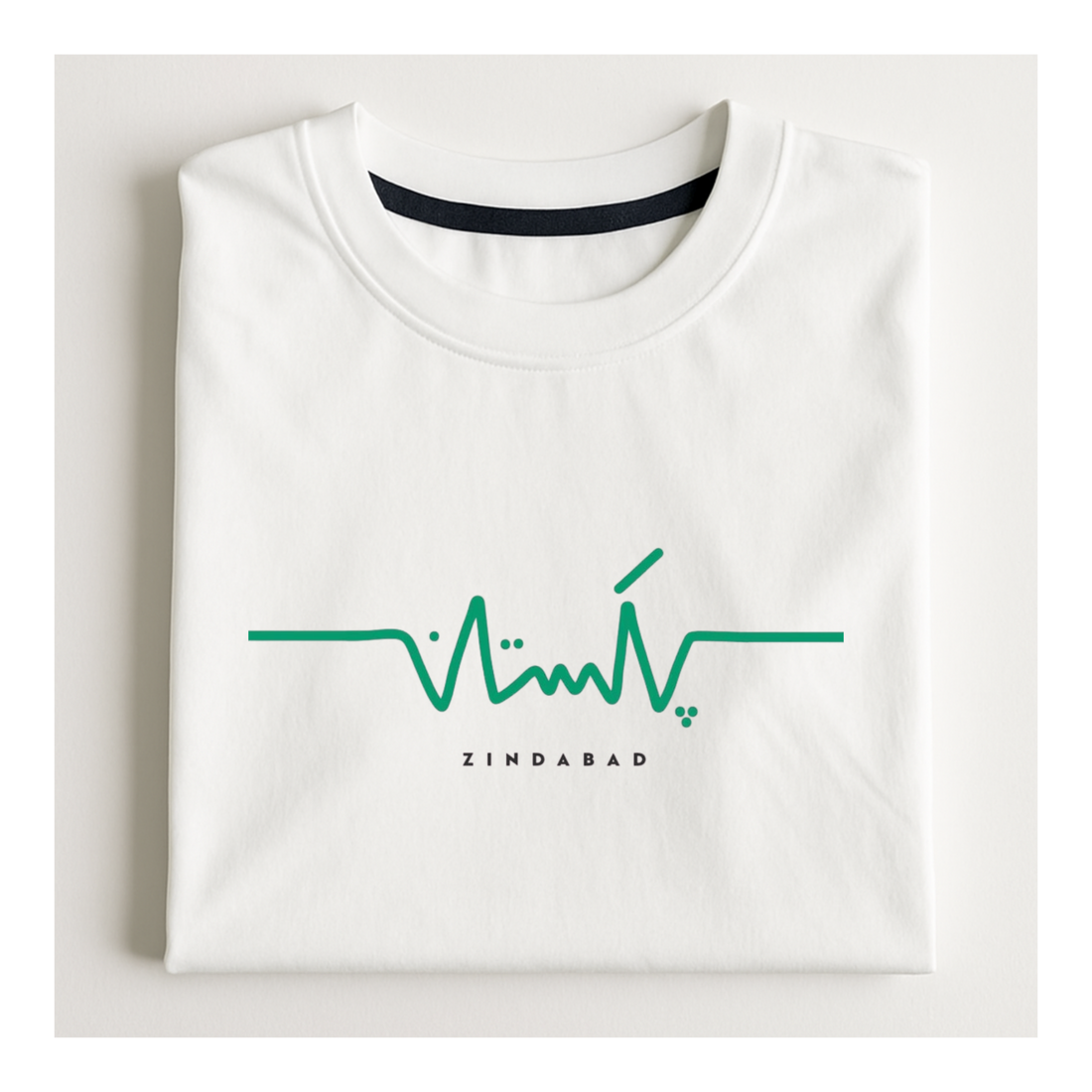 A folded white crewneck t-shirt with a green heartbeat line graphic and the word 'ZINDABAD' printed in black below it, displayed on a light off-white background.
